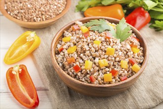 Buckwheat porridge with vegetables in wooden bowl on a white wooden background and linen textile.