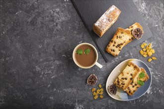 Homemade cake with raisins, dried persimmon and a cup of hot chocolate on a black concrete