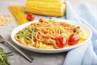 Corn noodles with tomato sauce and arugula on a gray concrete background and blue textile. Side