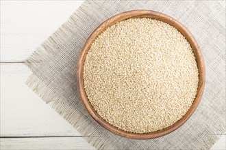 Wooden bowl with raw white quinoa seeds on a white wooden background and linen textile. Top view,