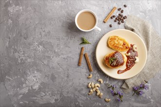 Cheese pancakes with caramel sauce on a beige ceramic plate and a cup of coffee on a gray concrete