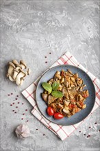 Fried oyster mushrooms with tomatoes on gray concrete background. Top view, copy space