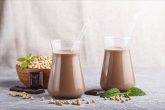 Organic non dairy soy chocolate milk in glass and wooden plate with soybeans on a gray concrete