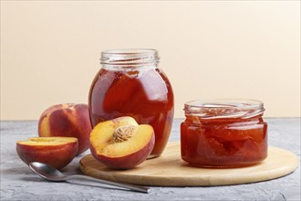 Peach jam in a glass jar with fresh fruits on gray concrete background. side view, close up