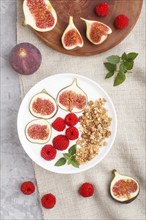 Yoghurt with raspberry, granola and figs in white plate on a gray concrete background and linen