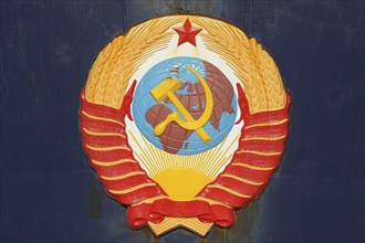 Soviet emblem featuring hammer and sickle over a globe, surrounded by wheat and topped with a red