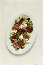 Salad with dried tomatoes, prosciutto, soft cheese, olives, homemade, top view