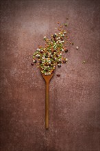 Wooden spoon, with an assortment of legumes, beans, peas, top view, on a brown background