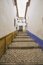 Old street with mosaic style paving stone stairs and white roughcast buildings with blue and yellow