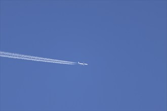 Aircraft in flight with a contrail or vapour trail across a blue sky, England, United Kingdom,