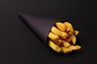 French fries, in black paper packaging, on a black background, close-up, selective focus