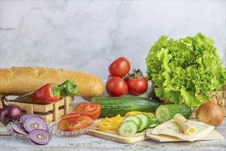 Colourful peppers, tomatoes and cucumber, some sliced, salad and cheese slices next to a baguette