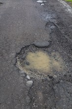 Pothole filled with rainwater on wet black asphalt road surface in spring, Montreal, Quebec,