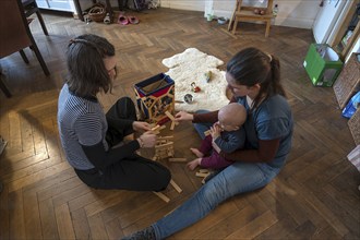 Young mother with her sister and with her son, 8 months, playing on the parquet floor,