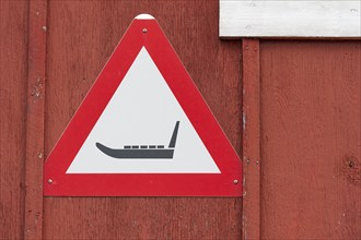 Triangular warning sign with sledge symbol on a red wooden wall, remote Arctic Inuit settlement