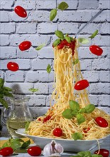 Spaghetti in a bowl and on a floating fork surrounded by tomatoes, basil and garlic