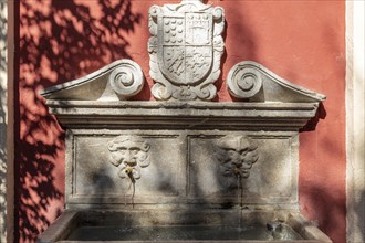 Decorated stone fountain with coat of arms and water feature on a shaded background, Granada