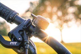 Bicycle handlebars with bell in the sunset, nature and trees in the background, forest bike,