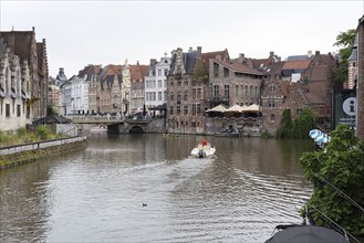 A boat sails along a quiet canal past historic buildings under a grey sky, Ghent