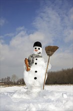 Decorated snowman with carrot nose, hat, pipe, scarf and broom in the snow in winter