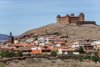 Medieval castle on a hill above a small town with colourful houses and a church, clear, sunny