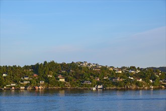 Small wooded island with houses in the sea with clear skies and calm water, Strusshamn, Bergen,