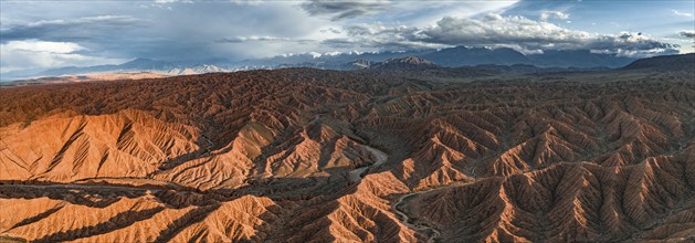 River bed runs through a landscape of eroded hills, badlands at sunset, mountain peaks of the Tian