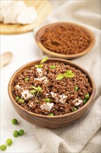 Quinoa porridge with green pea and chicken in wooden bowl on a white wooden background and linen