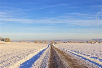 Long straight country road with ice and snow on the roadway in a beautiful wintry rural landscape