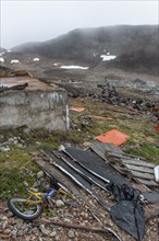 Broken children's bicycle, pallets, plywood, junkyard in rocky, hilly landscape with snow remains,