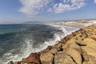 Rocky coastline with crashing waves and a sweeping view across the sea to the town in the