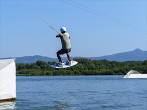 Young man jumping with wakeboard over jump into the lake, water sports, water skiing in wakepark,