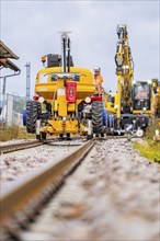 Construction workers operate yellow machines along the tracks on a construction site, track