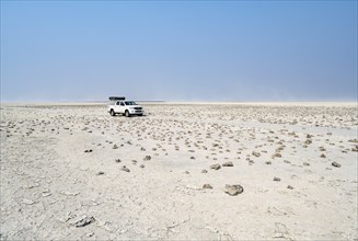 Four-wheel drive Toyota Hilux with roof tent, driving over salt pan, lone car in large wide plain,