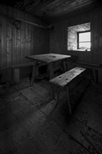 Rustic wooden hut with simple table and benches, illuminated from a window, Tyrol, Austria, Europe