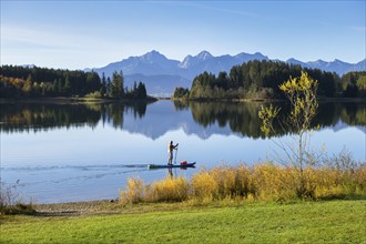 A quiet lake surrounded by mountains and forests with a person on a paddleboard in autumn,