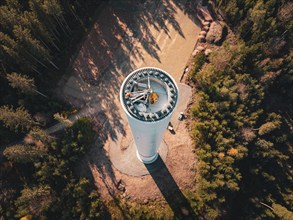 Sunlit wind turbine under construction with shadow cast, embedded in a forest landscape, wind