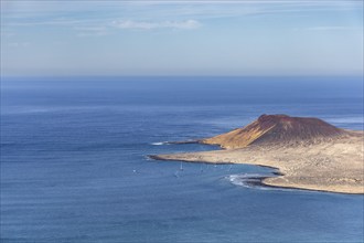 Landscape with island and volcanic crater on the coast and blue sea under clear sky, sailboats in