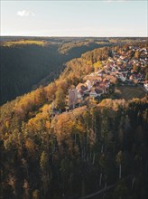 Small village with castle on a hill, surrounded by colourful autumn forest under a blue sky,