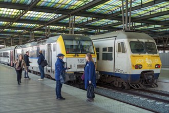 Passengers and two railway employees, ticket inspectors in front of waiting trains on platform at