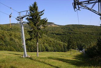 A cable car leads over a wooded hill under a clear blue sky in summer, Pezinska Baba ski resort,