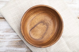 Empty wooden bowl on white wooden background and linen textile. Top view, flat lay, close up