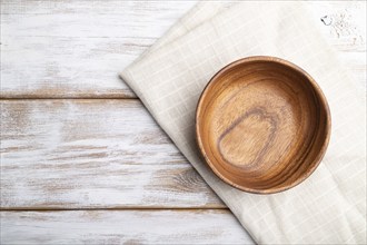 Empty wooden bowl on white wooden background and linen textile. Top view, flat lay, copy space