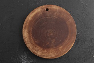 Empty round wooden cutting board on black concrete background. Top view, flat lay