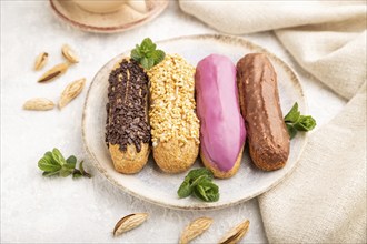 Set of eclair, traditional french dessert and cup of coffee on gray concrete background and linen