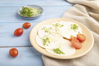 White cheese with tomatoes and cilantro microgreen on blue wooden background and linen textile.