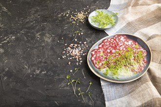 Slices of smoked cervelat salami sausage with spinach microgreen, salt and pepper on black concrete