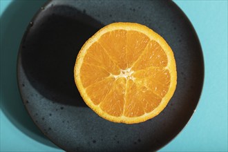 Ripe cut orange on blue ceramic plate on blue pastel background. Top view, flat lay, close up, hard