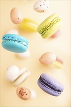 Multicolored flying macaroons and chocolate eggs frozen in the air on blurred beige background. top