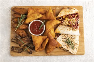 Set of snacks: nachos, chicken wings, fried ribs, bean tortillas on a cutting board on a gray